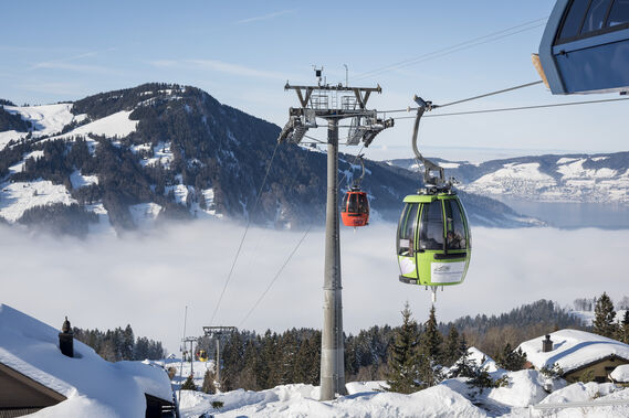 Schöner Wintertag. Blick von der Bergstation auf das Nebelmeer und zwei Gondeln, rot und grün.