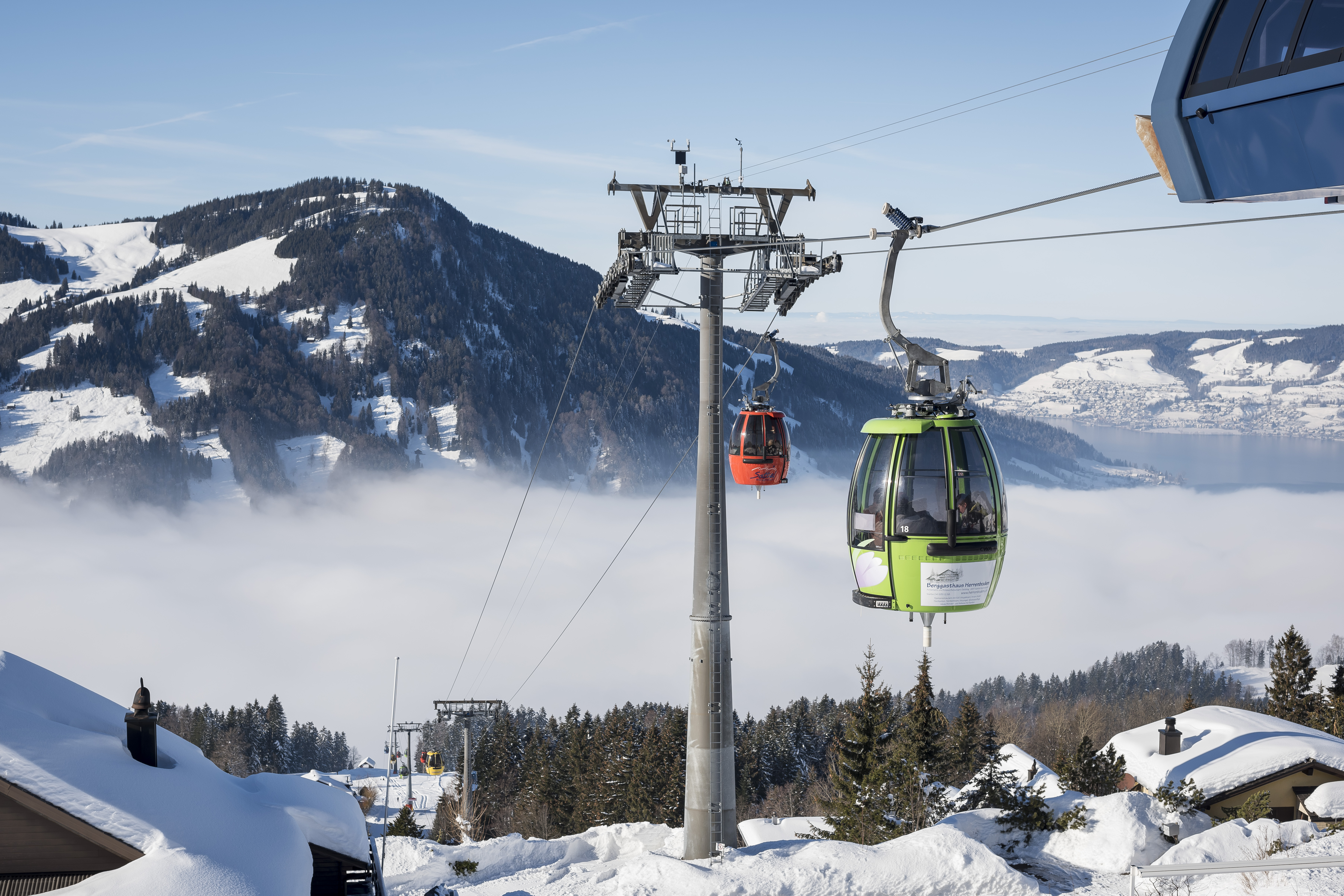 Schöner Wintertag. Blick von der Bergstation auf das Nebelmeer und zwei Gondeln, rot und grün.