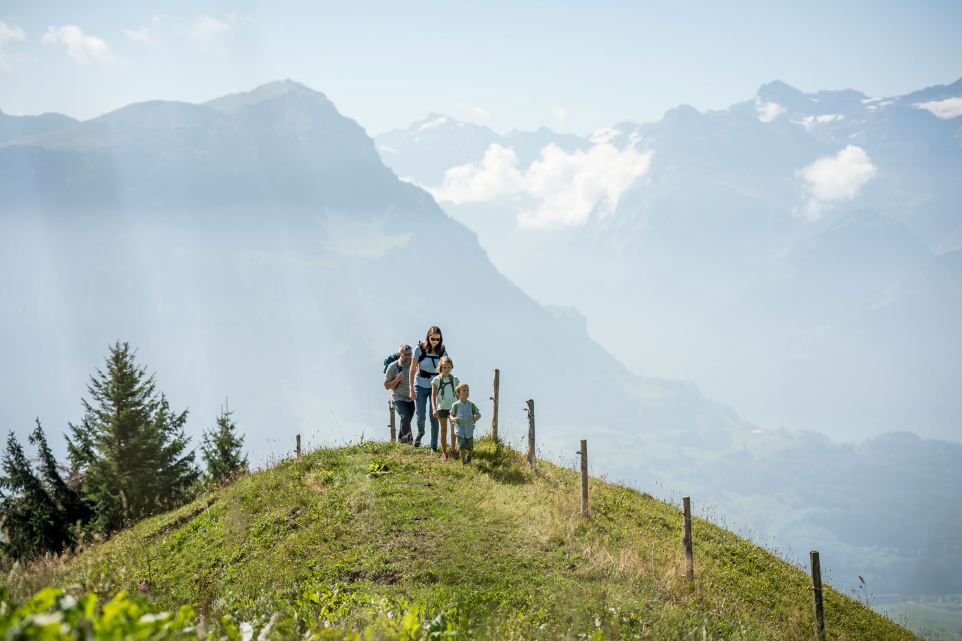 Eine Familie wandert über einen kleinen Hügel. Im Hintergrund sieht man Berge. 