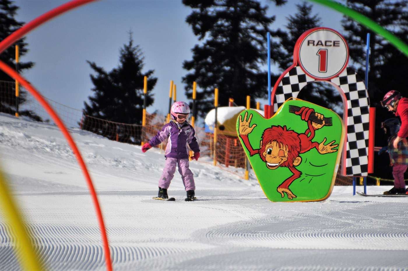 Kleinkind in violetter Skikleidung im Kinderland. 