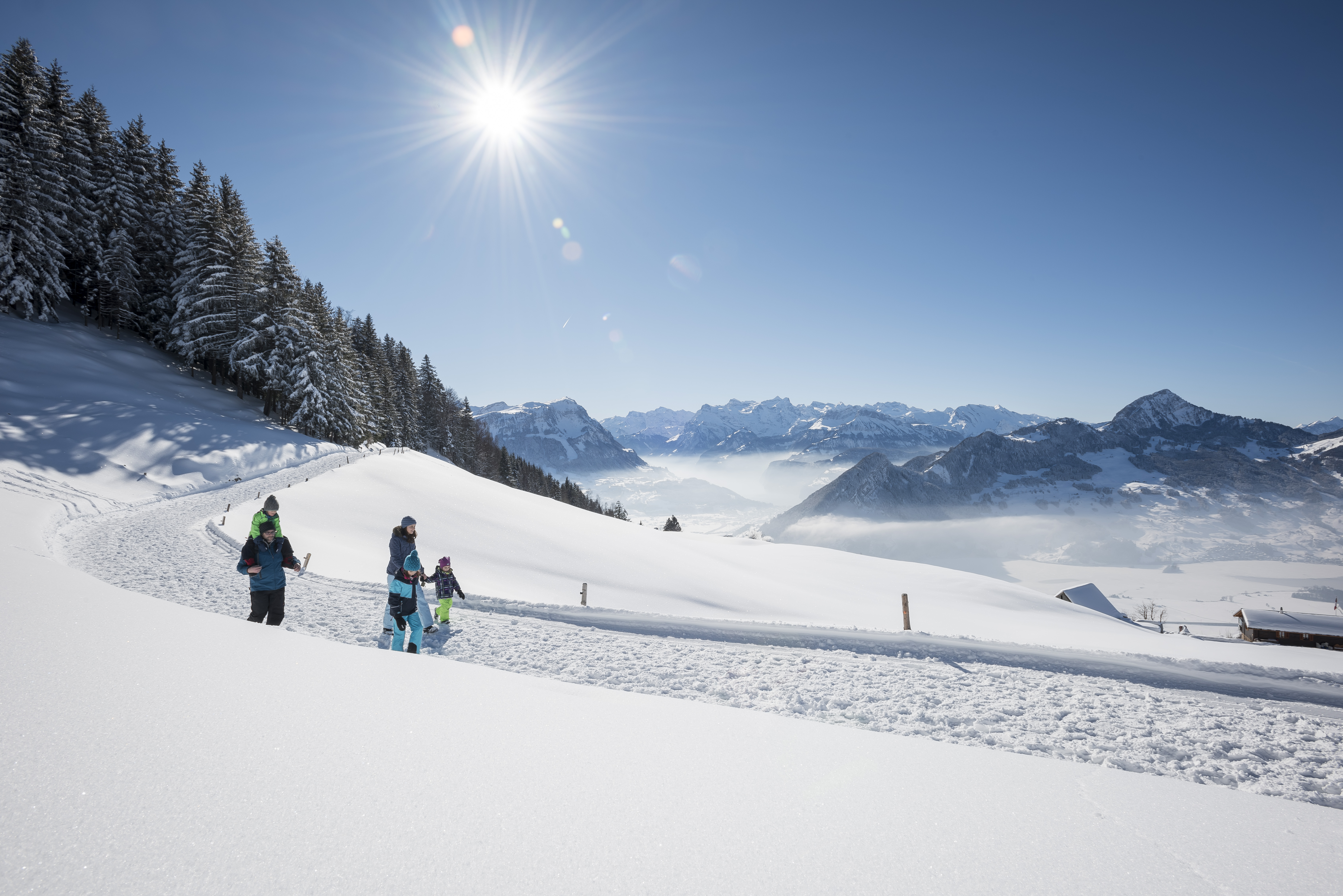 Winterrundweg. Eine Familie auf dem Wem bei schön sonnigem Wetter und Blick auf die Berge. 