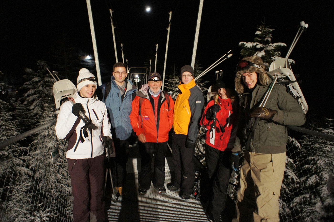 Eine Gruppe Schneeschuhwanderer auf der Hängebrücke bei Nacht. 