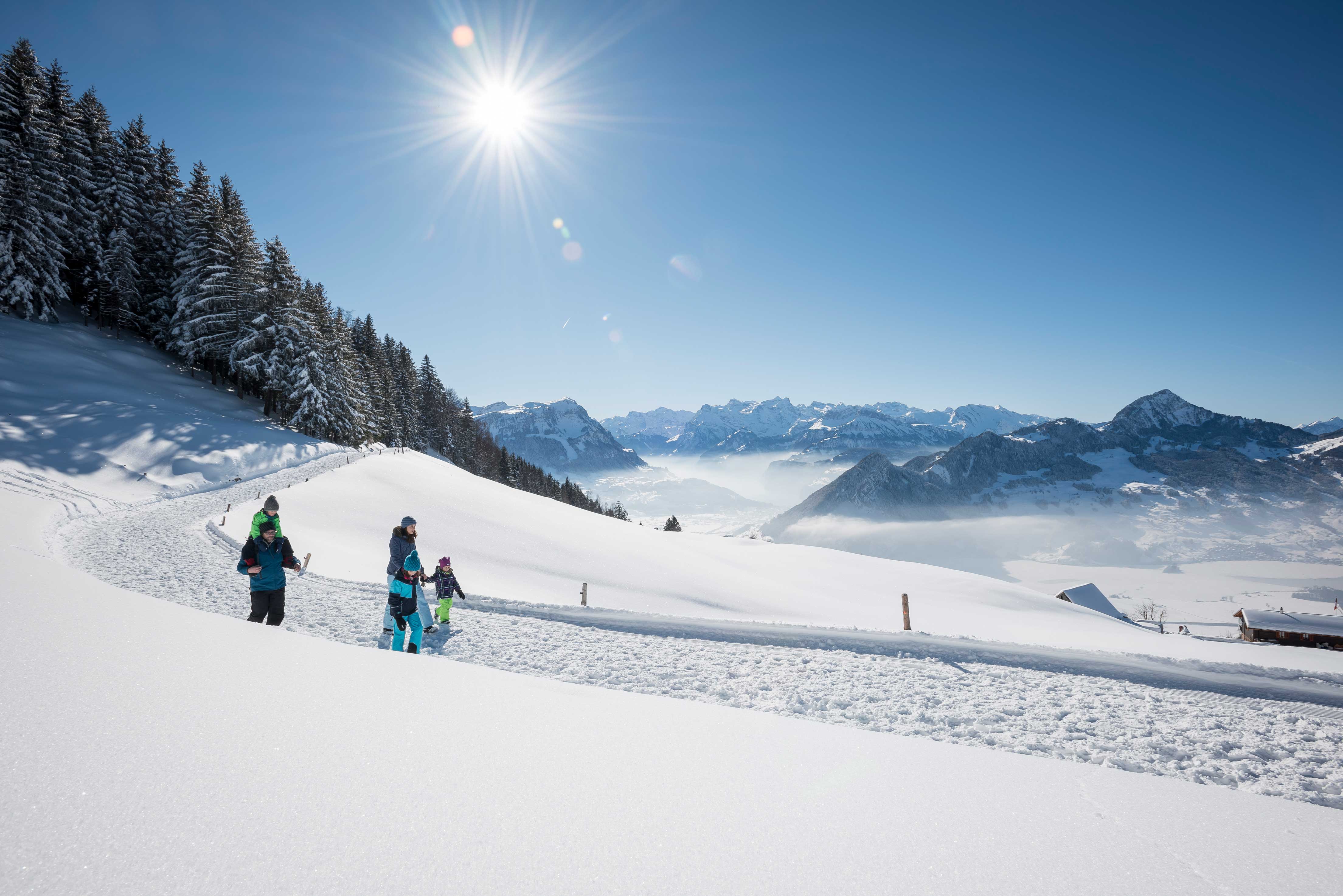 Winterrundweg. Eine Familie auf dem Wem bei schön sonnigem Wetter und Blick auf die Berge. 