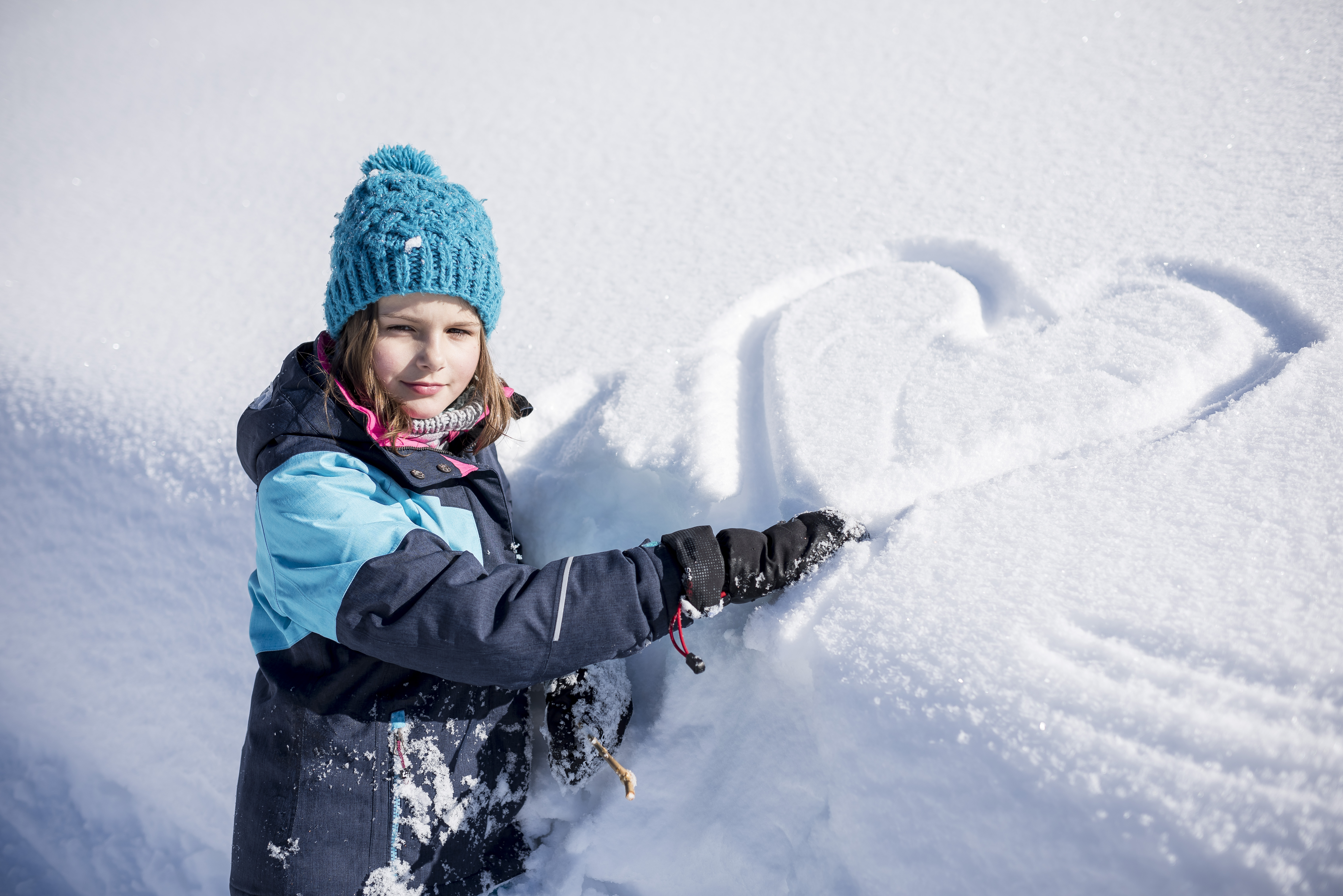 Ein Mädchen mit blauer Mütze hat ein Herz in den Schnee gemalt.