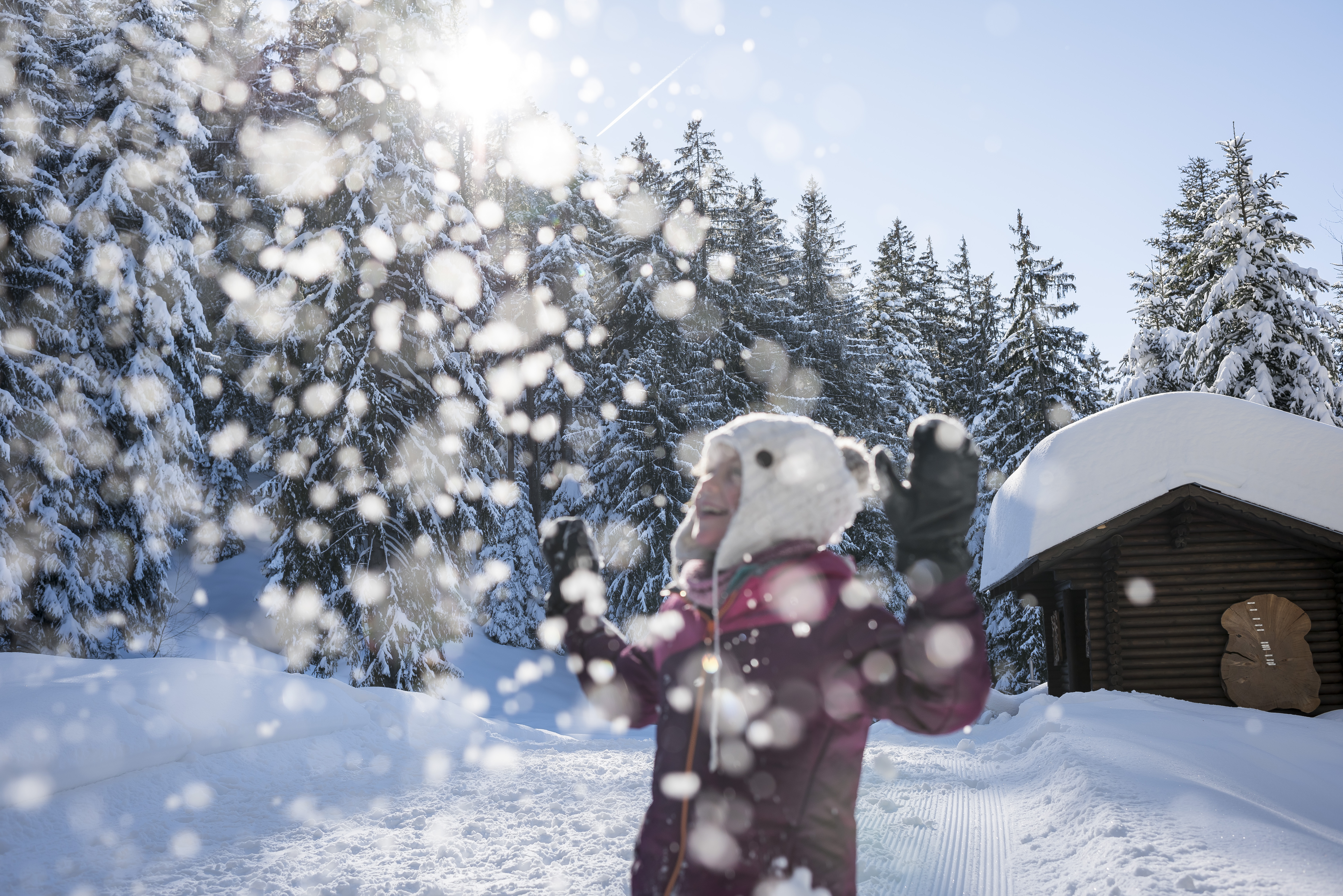 Ein Mädchen wirft bei einem verschneiten Wald Schnee in die Luft. 